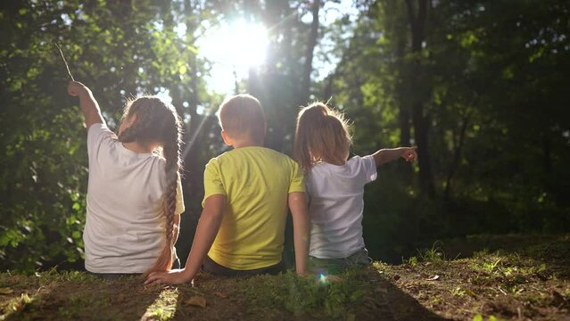 children sit on the banks of the river. happy family childhood dream concept. a group of little children sit together by the river and lifestyle talk. kids spend time outdoors in nature in the forest