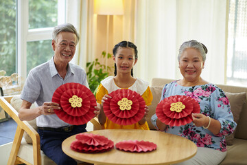 Teenage girl and her grandparents enjoying creating paper decorations for spring festival