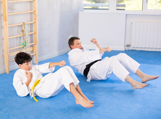 ..Adult man and boy teenager in kimono doing abdominal exercises in studio..