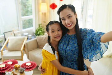 Portrait of hugging mother and daughter taking selfie after making Tet decorations