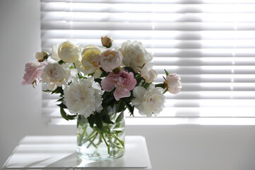 Beautiful peonies in vase on table near window indoors