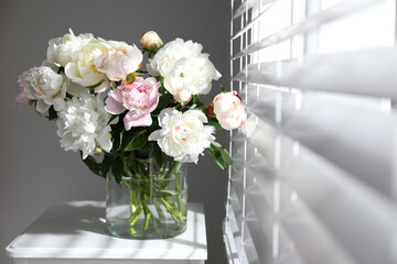 Beautiful peonies in vase on table near window indoors