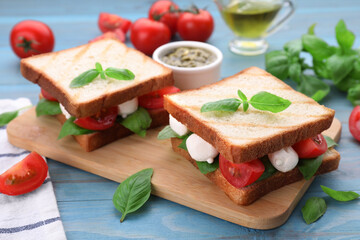Delicious Caprese sandwiches with mozzarella, tomatoes, basil and pesto sauce on light blue wooden table