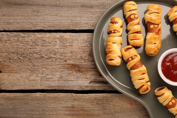 Cute sausage mummies served with ketchup on wooden table, top view with space for text. Halloween...