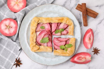 Delicious apple galette with mint and ingredients on white marble table, flat lay