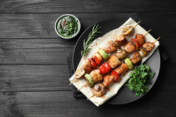 Delicious shish kebabs with vegetables served on black wooden table, flat lay. Space for text