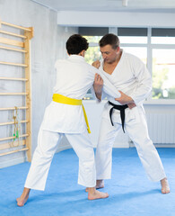 Adult man and teenage boy judokas practicing judo fighting in studio