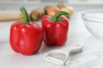 Red bell peppers and peeler on white marble table, closeup