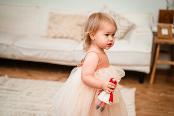 A tender two-year-old girl child in a magnificent elegant dress at home in a Christmas interior with a Christmas tree, New Year and Christmas concepts