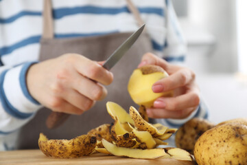 Woman peeling fresh potato with knife at table, focus on peels