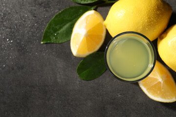 Tasty limoncello liqueur, lemons and green leaves on grey table, top view. Space for text