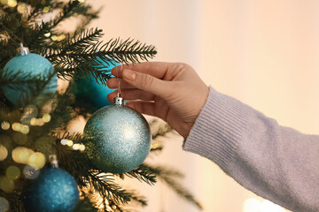 Woman decorating Christmas tree with light blue festive ball on blurred background, closeup