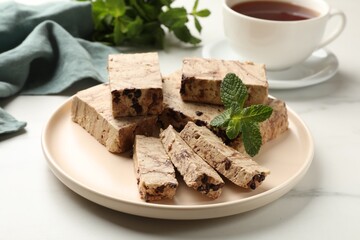 Pieces of tasty chocolate halva and mint served on white marble table, closeup