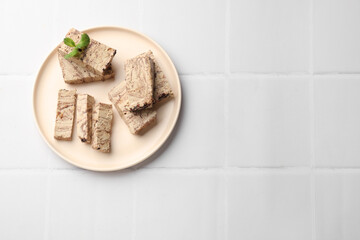 Tasty chocolate halva with mint on white tiled table, top view