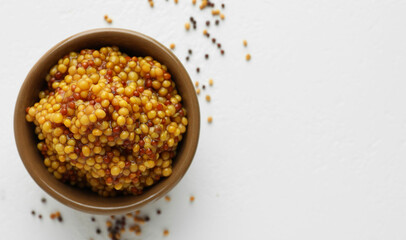 Fresh whole grain mustard in bowl and dry seeds on white table, flat lay. Space for text