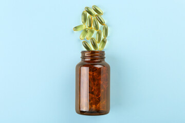 Bottle and vitamin capsules on light blue background, top view