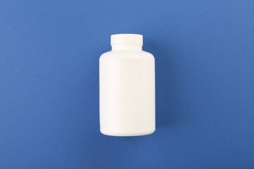 Blank white pill bottle on blue background, top view. Space for text