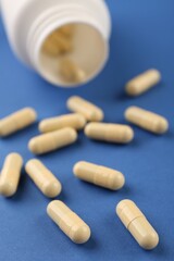 Bottle and vitamin capsules on blue background, closeup