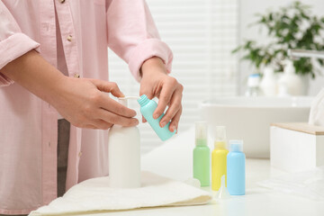 Obraz na płótnie Canvas Woman pouring cosmetic product into plastic bottle at white countertop in bathroom, closeup. Bath accessories
