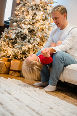 Young father man and baby child toddler have fun at home in front of the Christmas tree, New Year's home decor. Festive family atmosphere. 