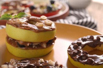Fresh apples with nut butter, peanuts and chocolate chips on plate, closeup
