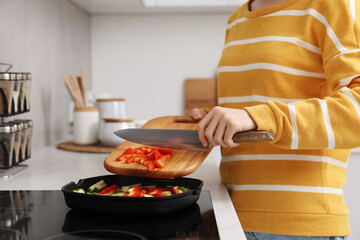 Cooking process. Woman adding cut bell pepper into pan with vegetables in kitchen, closeup