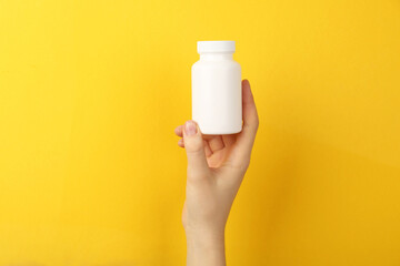 Woman holding blank white jar of vitamins on yellow background, closeup. Space for text - obrazy, fototapety, plakaty