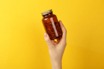 Woman holding jar with vitamin capsules on yellow background, closeup