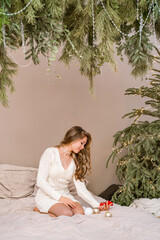 Cute young girl in beautiful curls at home on the bed in front of the Christmas tree. Beautiful concept of New year and Christmas, cozy festive atmosphere