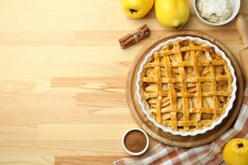Tasty homemade quince pie and ingredients on wooden table, flat lay. Space for text