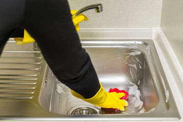 woman in rubber gloves washes the sink in the kitchen
