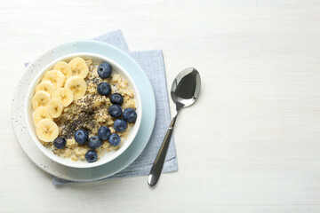 Tasty oatmeal with banana, blueberries and chia seeds served in bowl on white wooden table, flat lay. Space for text