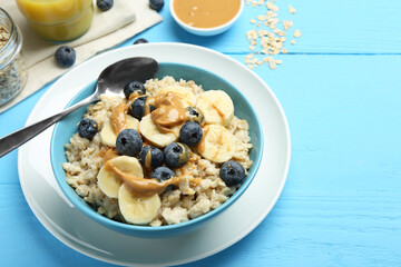 Tasty oatmeal with banana, blueberries and peanut butter served in bowl on light blue wooden table, space for text