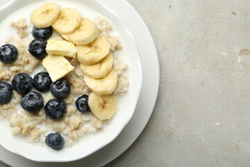 Tasty oatmeal with banana, blueberries, butter and milk served in bowl on light grey table, top view. Space for text