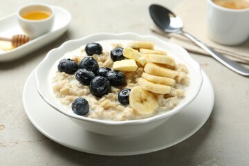Tasty oatmeal with banana, blueberries, butter and milk served in bowl on light grey table