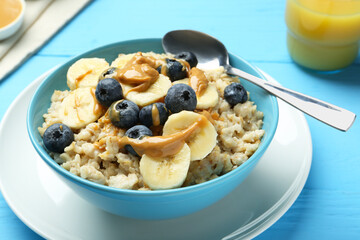 Tasty oatmeal with banana, blueberries and peanut butter served in bowl on light blue wooden table