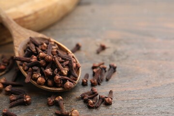 Spoon with aromatic cloves on wooden table, closeup. Space for text