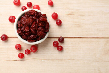 Dried cranberries in bowl and fresh berries on wooden table, top view. Space for text