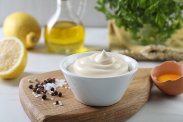 Tasty mayonnaise sauce in bowl, ingredients and spices on white table, closeup