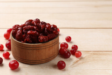 Dried cranberries in bowl and fresh berries on wooden table, space for text