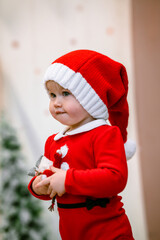 Cute baby toddler girl child in a red suit and santa hat during the Christmas holiday at home. Selective focus. The concept of New year and Christmas, the atmosphere of fun and comfort.