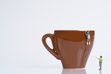 a mountaineer climbs a brown coffee cup, miniature figure scene