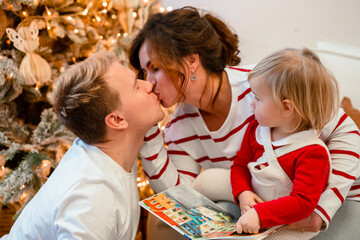 Young parents man and woman and baby child toddler have fun at home in front of the Christmas tree, New Year home decor. Festive family atmosphere. Samara, Russia - 30 Dec 2023