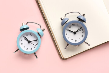 Alarm clocks and notebook on pink background, closeup