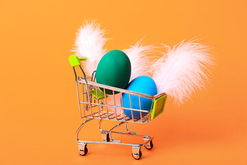 Shopping cart with Easter eggs and feathers on orange background