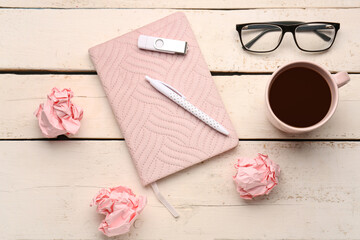 Composition with notebook, cup of coffee, eyeglasses, pen and crumpled paper balls on light wooden background