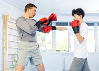 Sportive middle-aged man and teenage boy training boxing in pair during sports classes