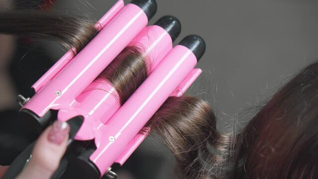Using electric curling iron to create wavy hair.