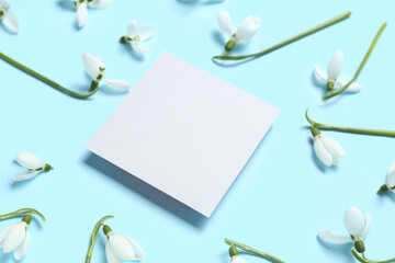 Fototapeta na wymiar Beautiful snowdrops and blank greeting card on blue background