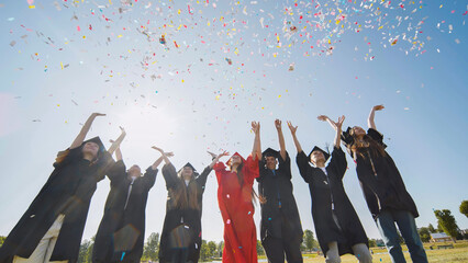 Happy college graduates throw colorful confetti against the rays of sunshine.
